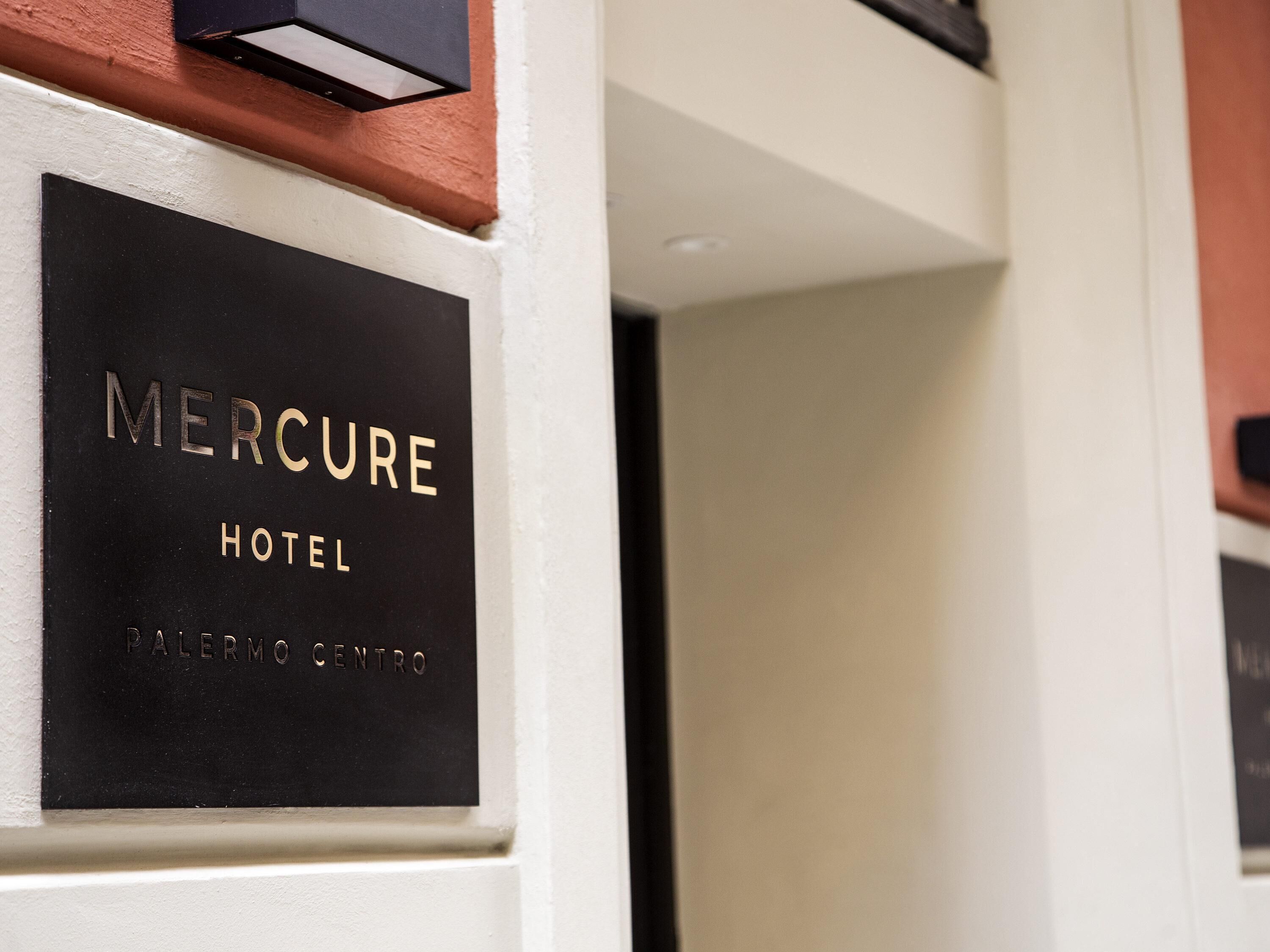 A black sign with 'MERCURE HOTEL' and 'PALERMO CENTRO' on a white wall.