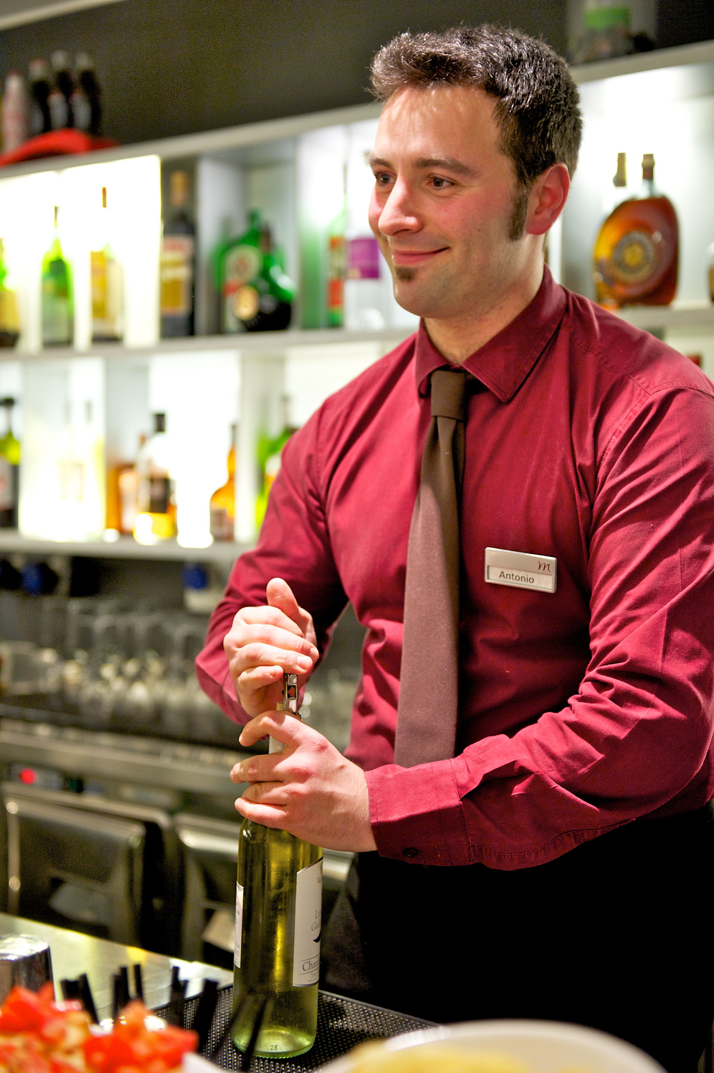 Una persona con camisa y corbata roja en un bar, sosteniendo una botella de vino.