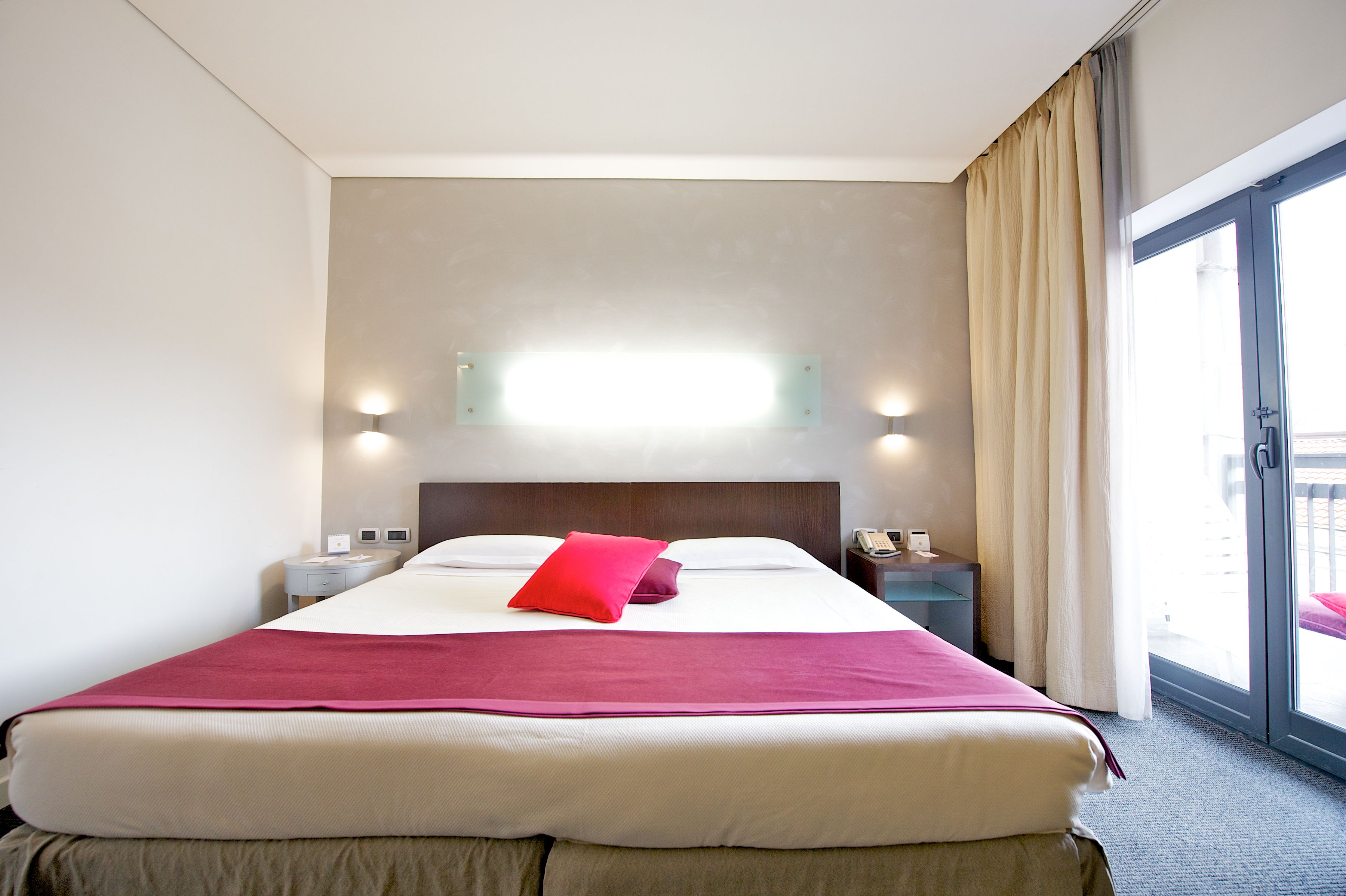 Habitación de hotel con una cama grande, una mesita de noche con teléfono y una ventana con cortinas.