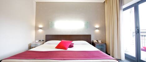 Habitación de hotel con una cama grande, una mesita de noche con teléfono y una ventana con cortinas.
