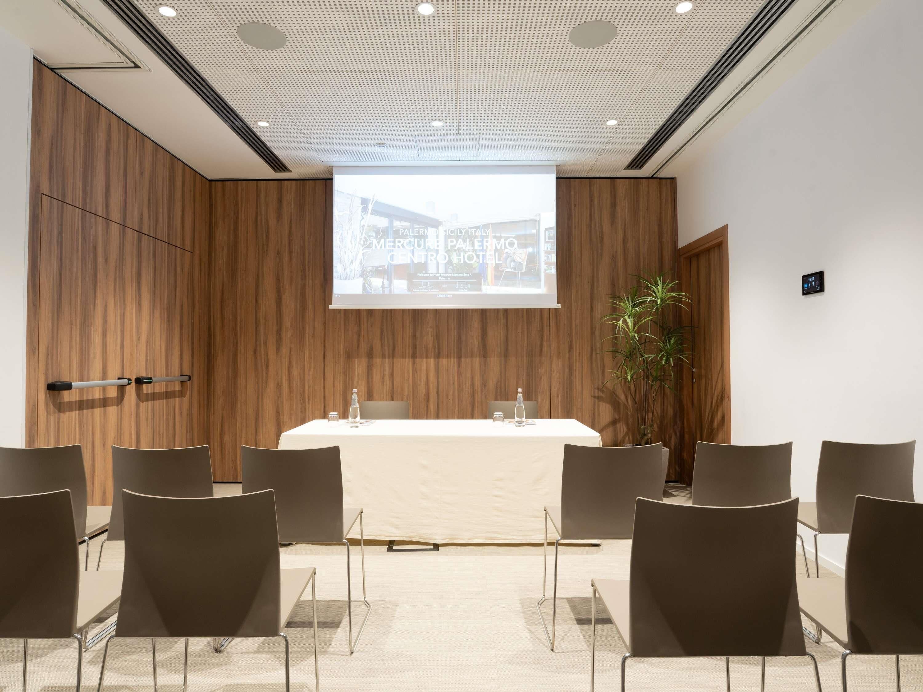Ein Konferenzraum mit einem langen Tisch, Stühlen, einer Projektionsleinwand und einer Holzwand.