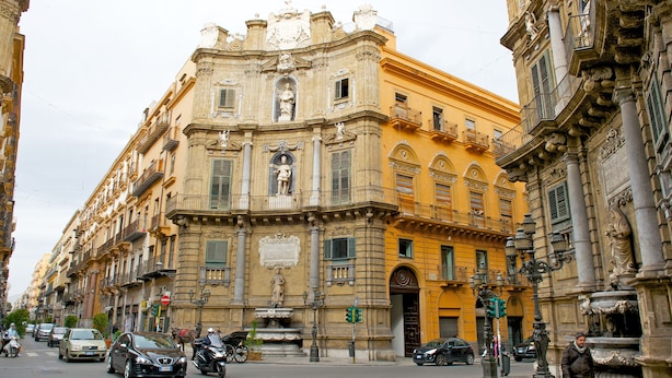 Un edificio histórico con arquitectura clásica, una fuente y una calle con coches y peatones.