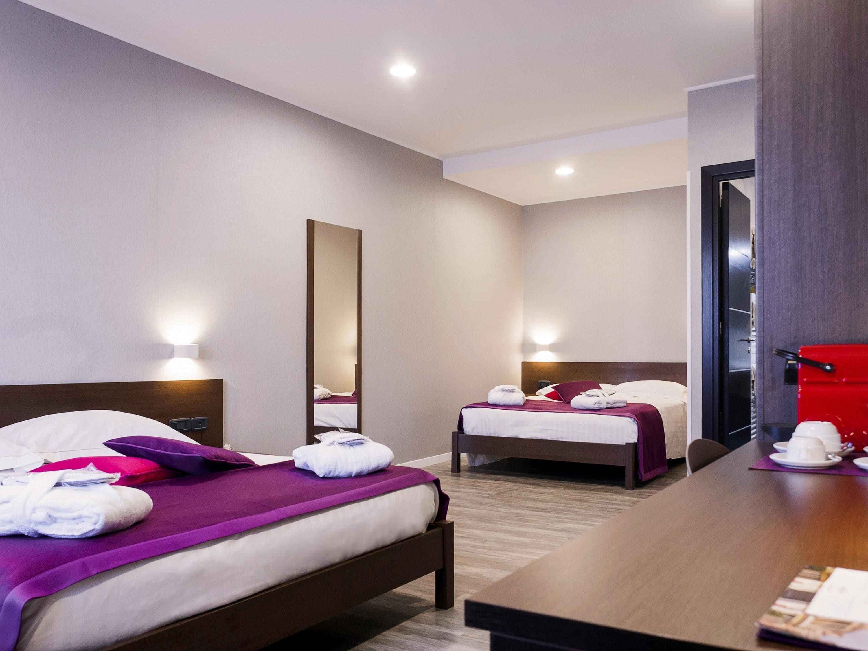 Une chambre d’hôtel avec deux lits, un grand miroir, des lampes de chevet, une table en bois et une poubelle rouge.