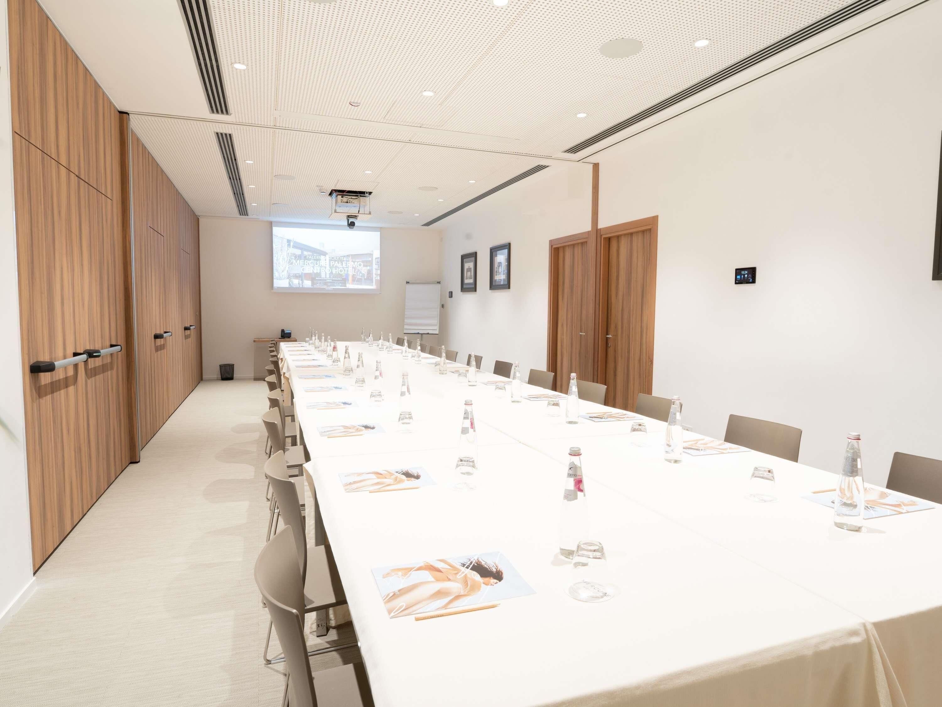 A conference room with a long table, chairs, and a projector screen.