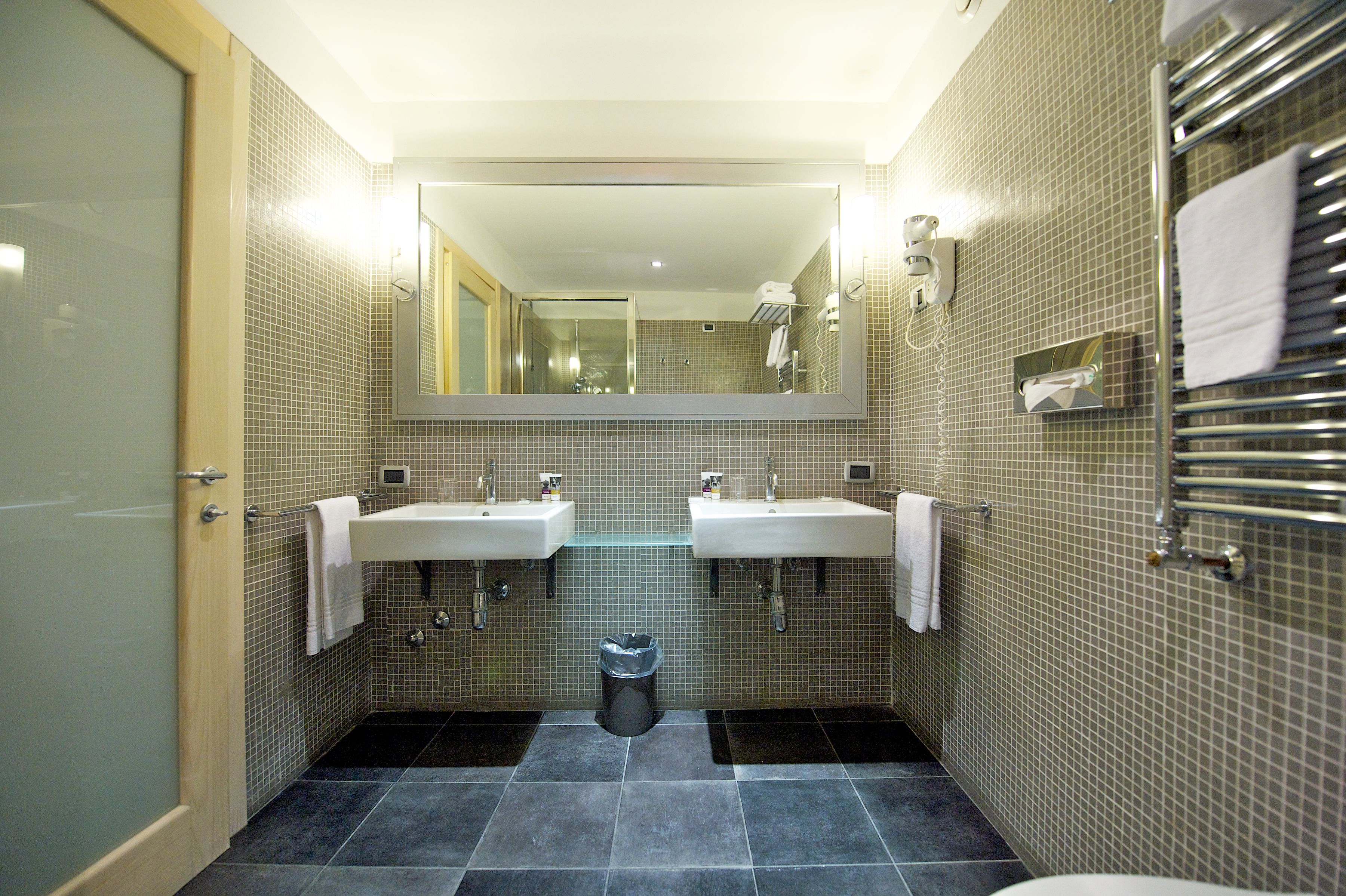 Une salle de bain moderne avec deux lavabos, un miroir et une poubelle.