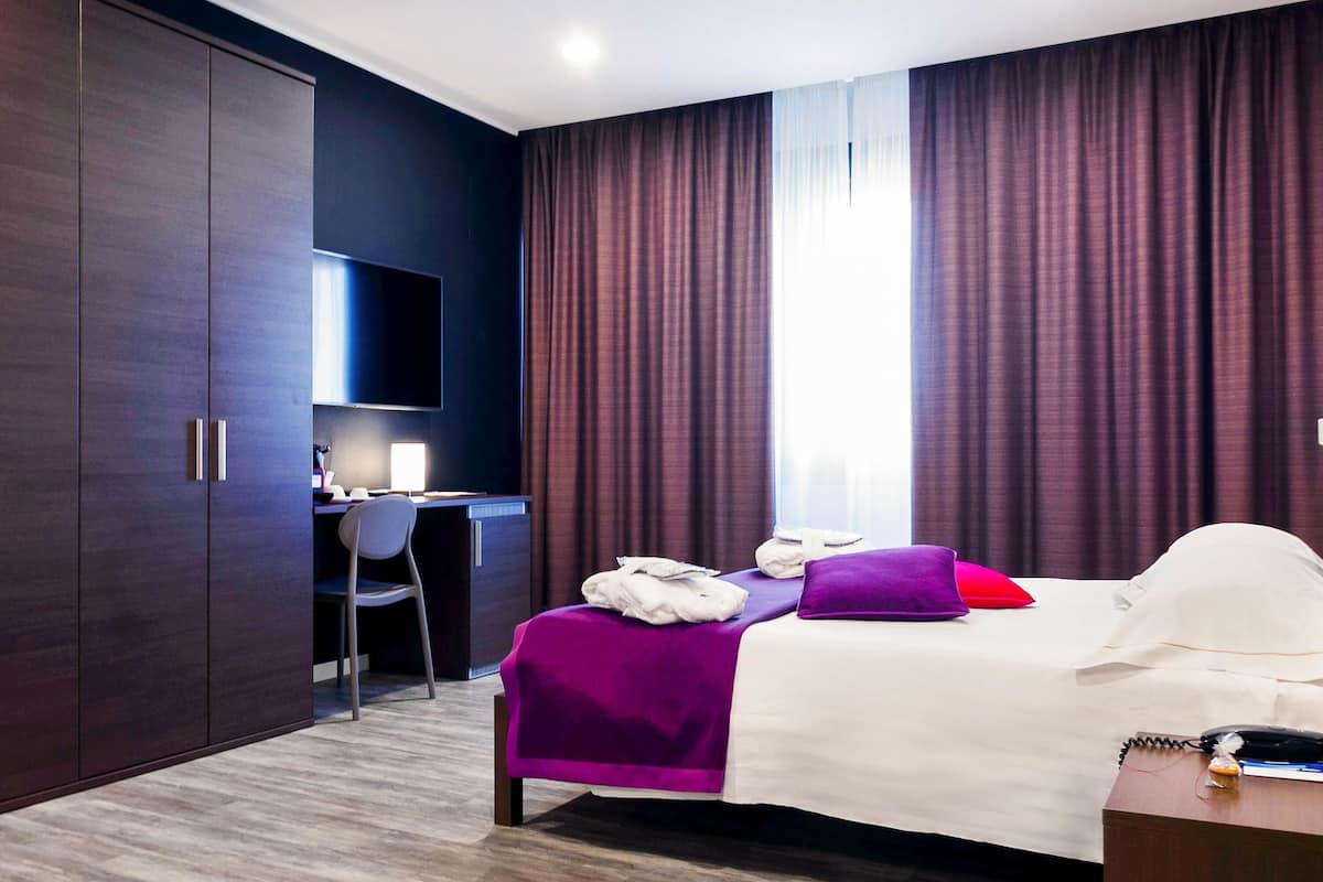 A hotel room with a bed, a desk, a chair, a TV, and a wardrobe.