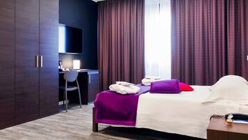 A hotel room with a bed, a desk, a chair, a TV, and a wardrobe.