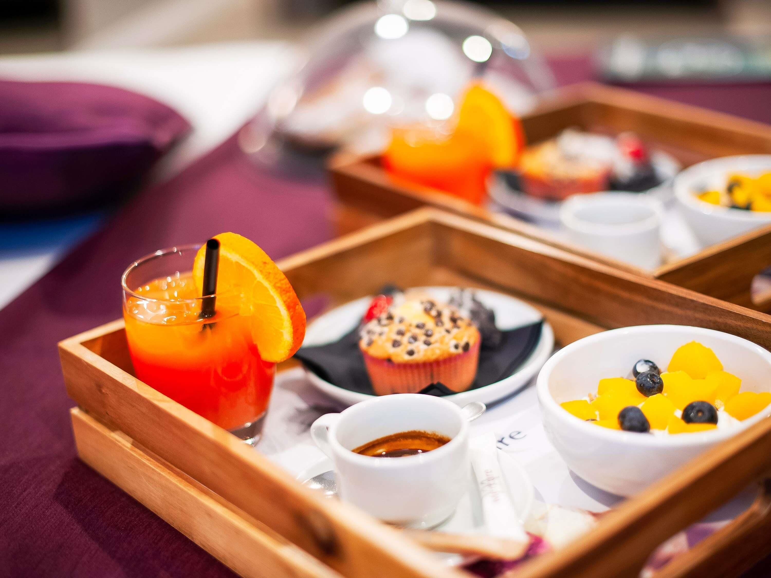 A tray with a glass of orange juice, a muffin, a bowl of fruit, and a cup of coffee.