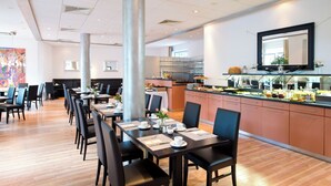 Un espace repas moderne avec de longues tables, des chaises noires et un comptoir de buffet.
