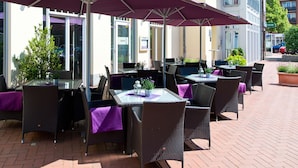 Un espace extérieur aménagé avec des tables et des chaises, dont certaines sont protégées par des parasols.