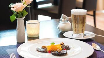 A dessert plate with a chocolate tart, orange slice, and nuts on a white plate, a candle, and a latte macchiato on a saucer.