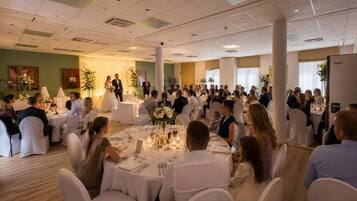 A banquet hall with round tables, white chairs, and guests seated for a reception.