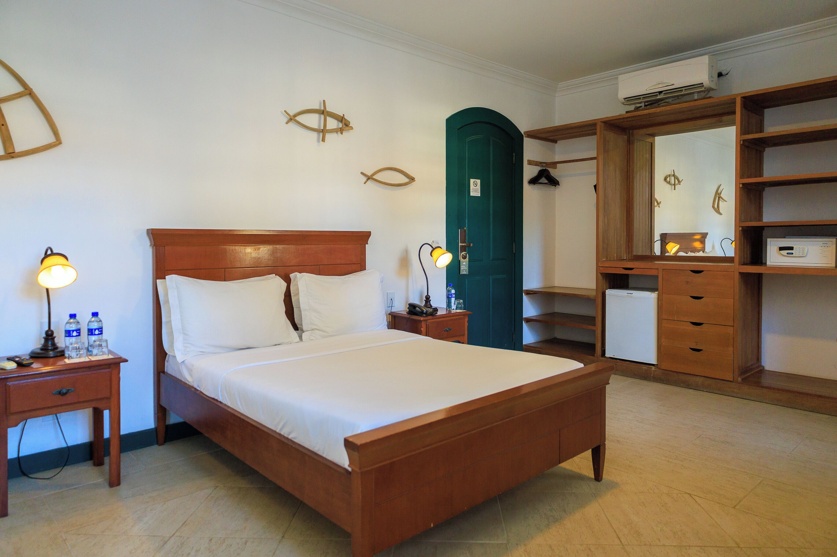 A hotel room with a wooden bed, bedside tables with lamps, a wardrobe, and a small refrigerator.