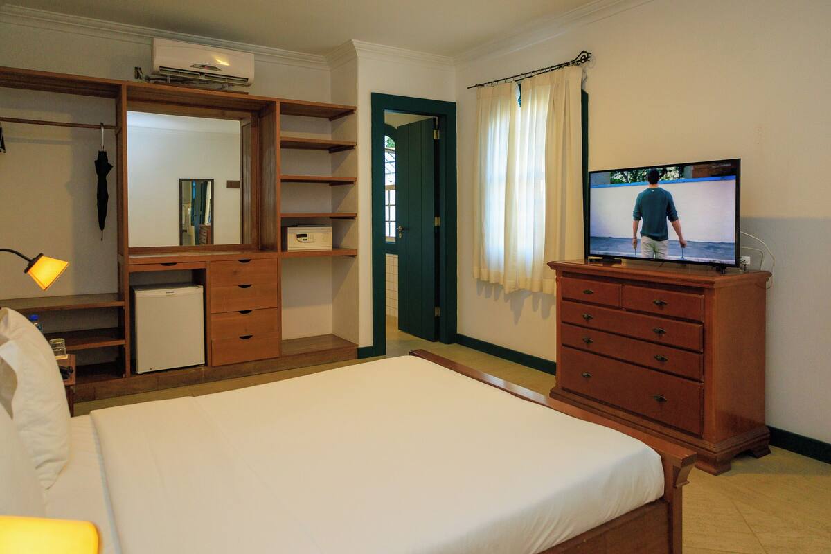 Habitación de hotel con cama, televisión, cómoda, escritorio con lámpara y armario.
