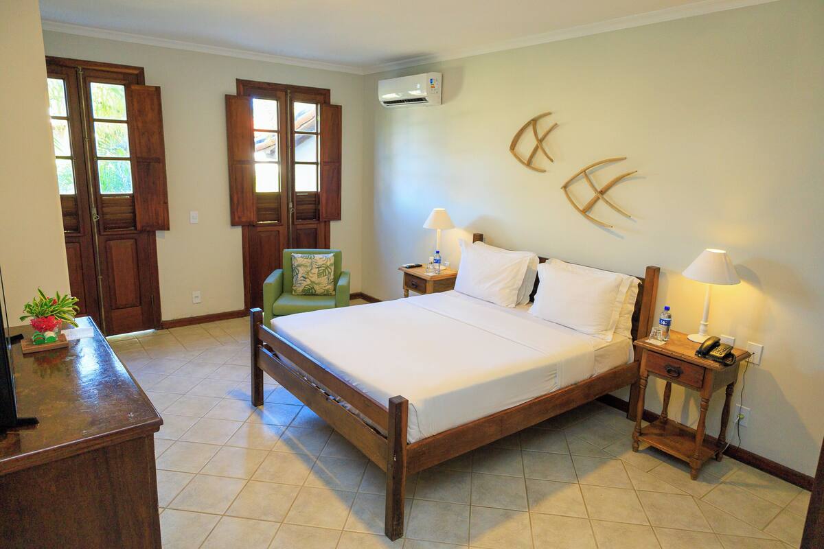 Un dormitorio con una cama de madera, una mesita de noche con lámpara, una silla y un escritorio con una planta.