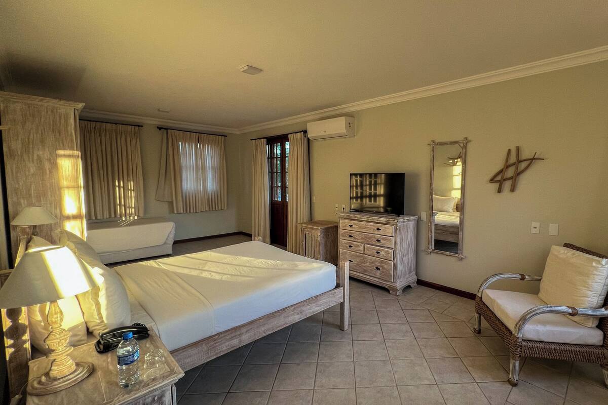 Una habitación de hotel con una cama, un aparador, una silla, un espejo y una ventana con cortinas.