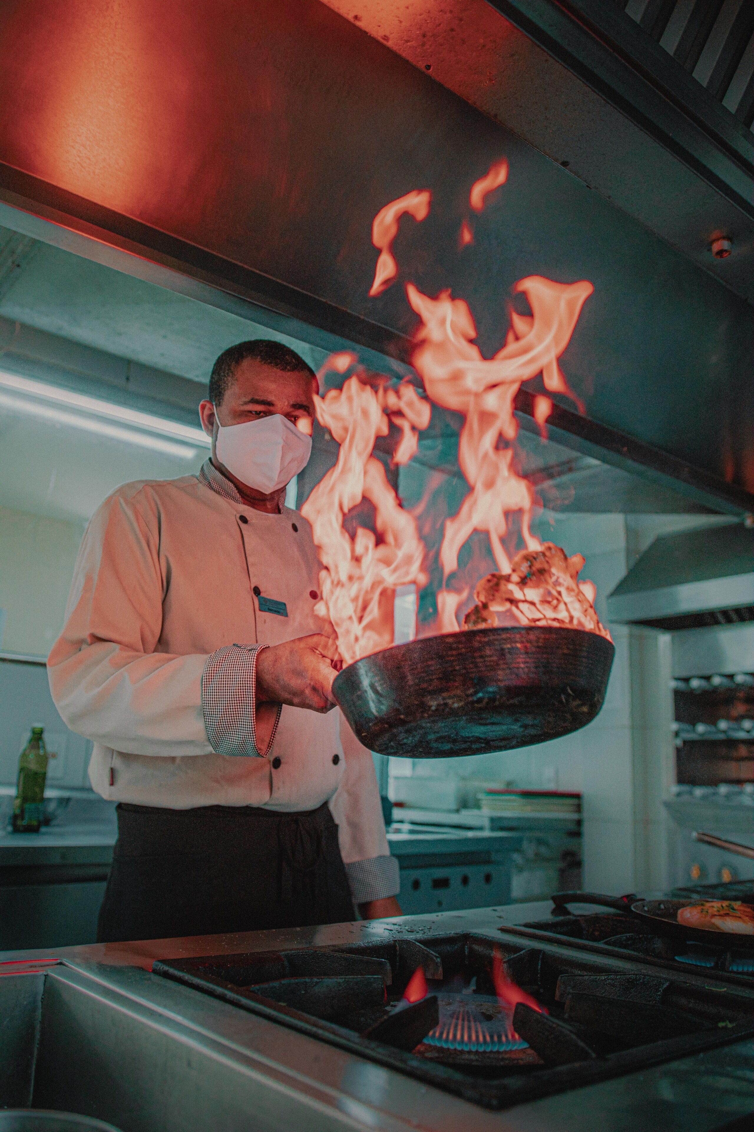 A chef holding a pan with food over a stove with flames.