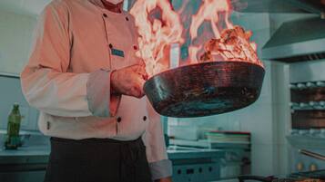 A chef holding a pan with food over a stove with flames.