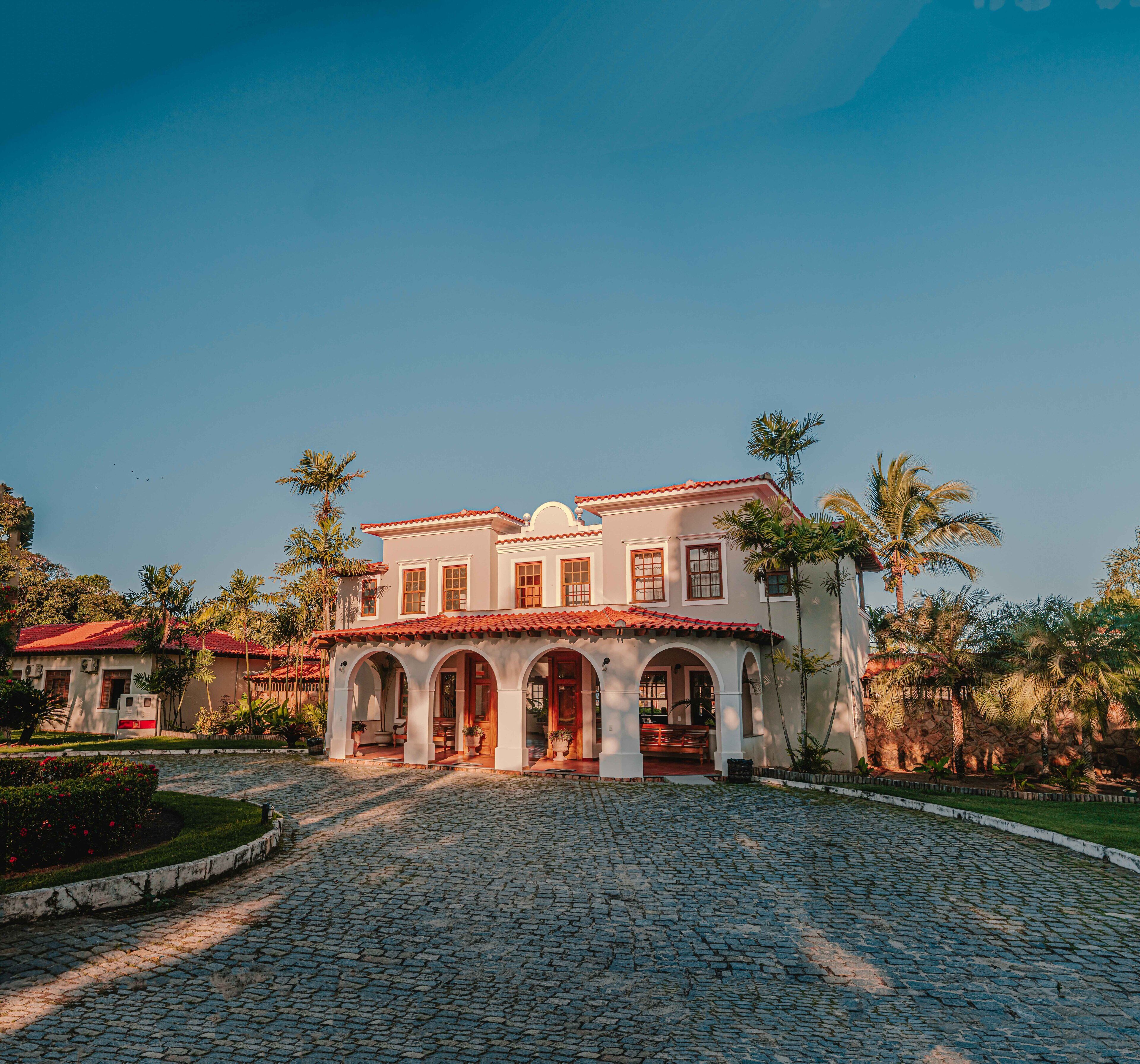 A two-story building with a red-tiled roof, multiple arches, and a cobblestone driveway.