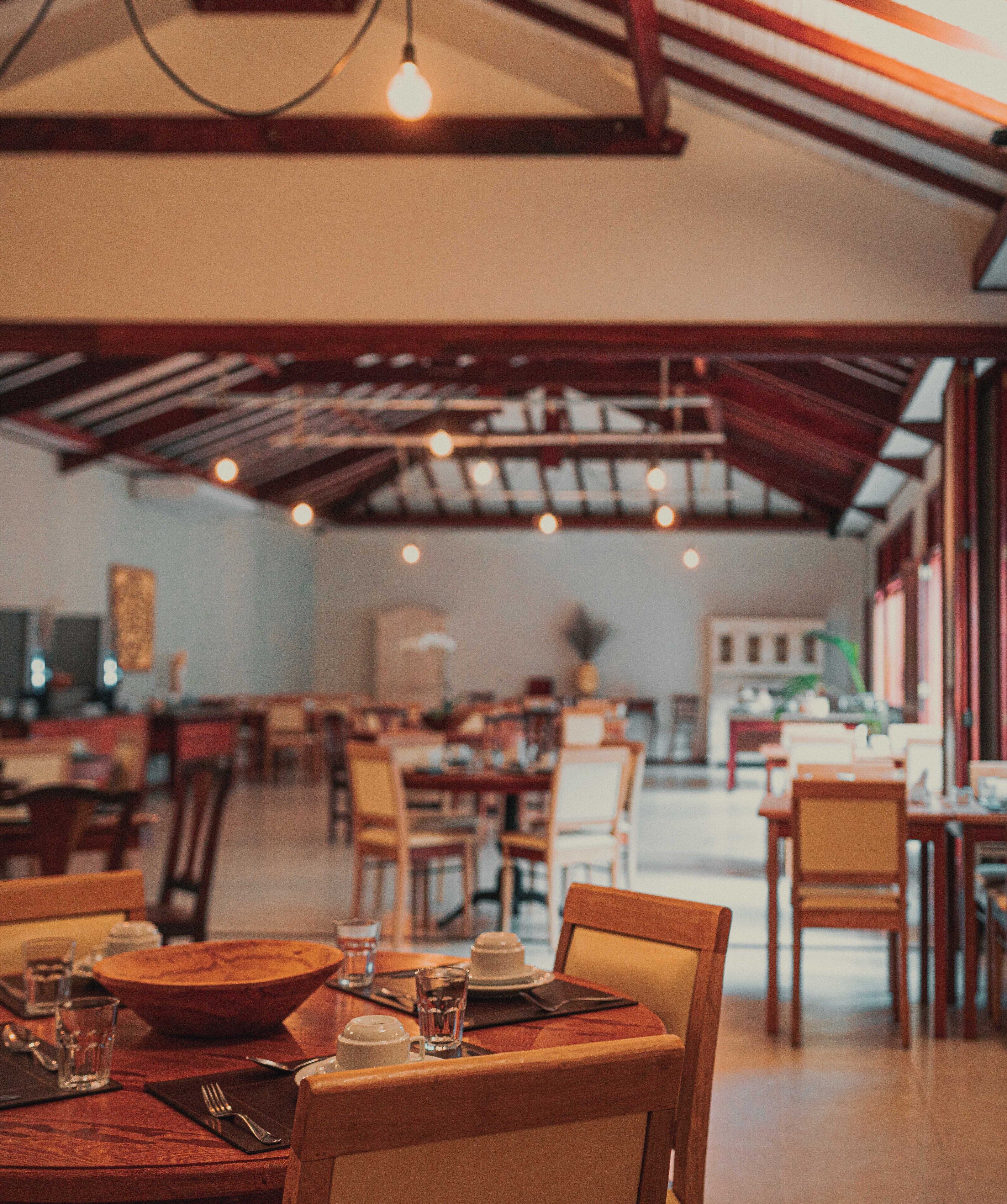 A restaurant with wooden tables and chairs, hanging lights, and a view of the dining area.