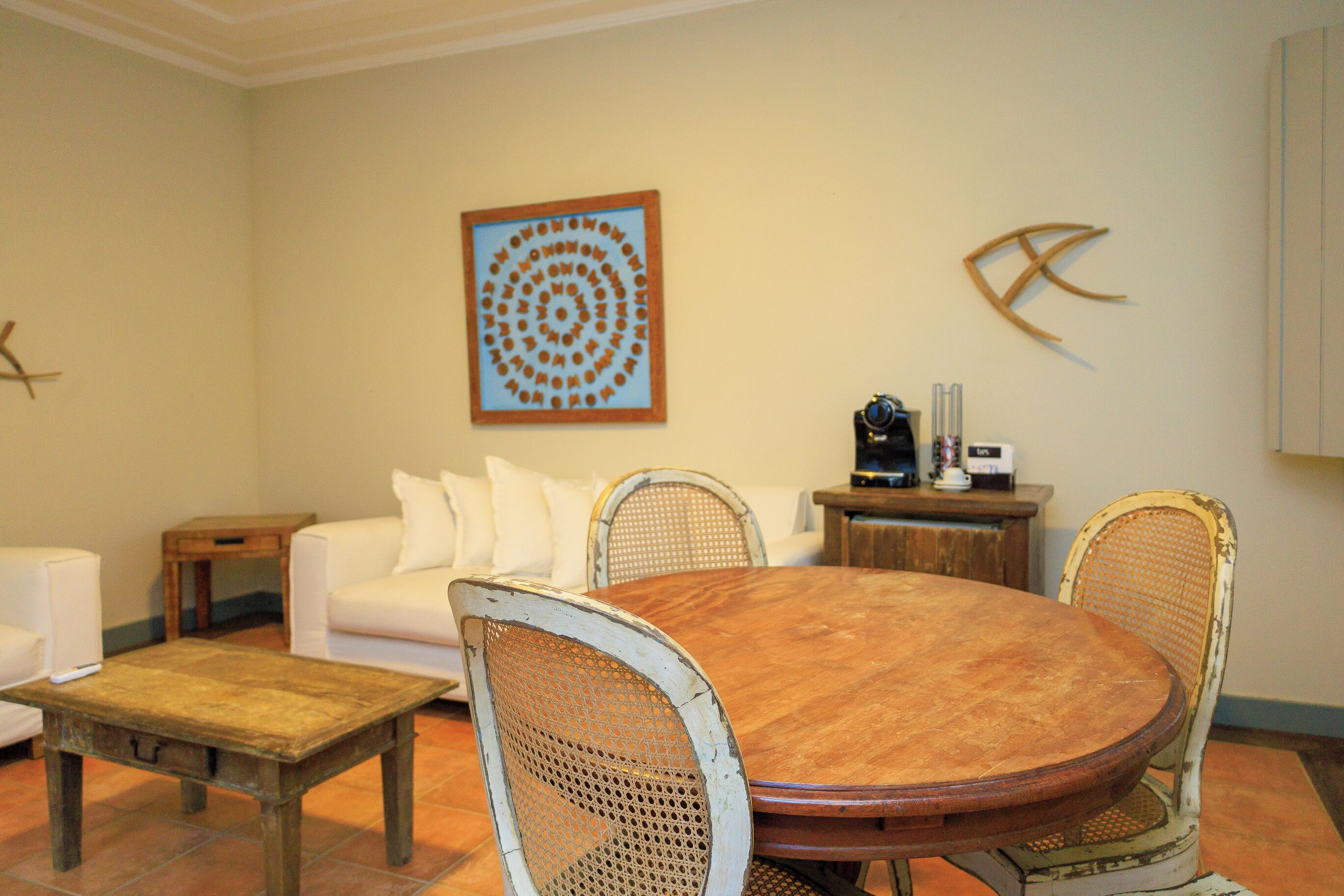 A dining area with a wooden table and wicker chairs, a white sofa, and a decorative wall piece.