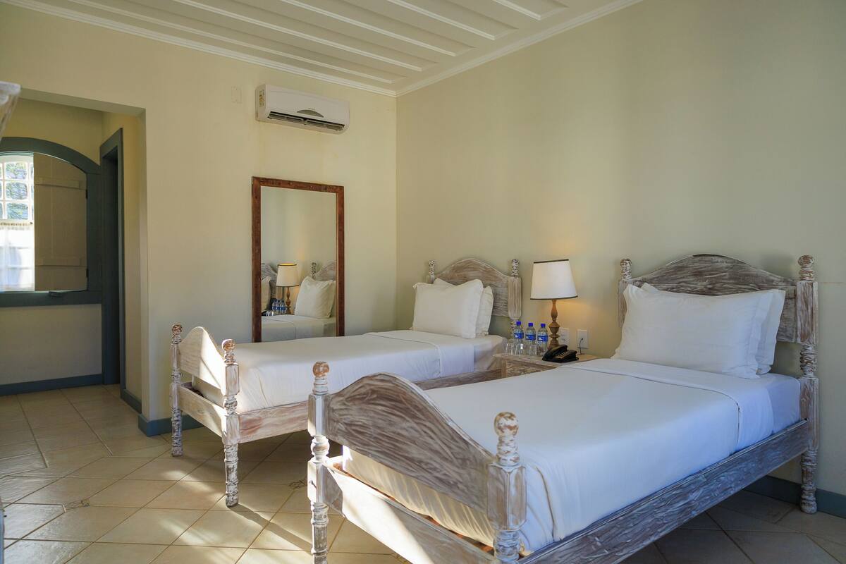 Habitación de hotel con dos camas, un espejo, una mesita de noche con lámpara y un equipo de aire acondicionado.