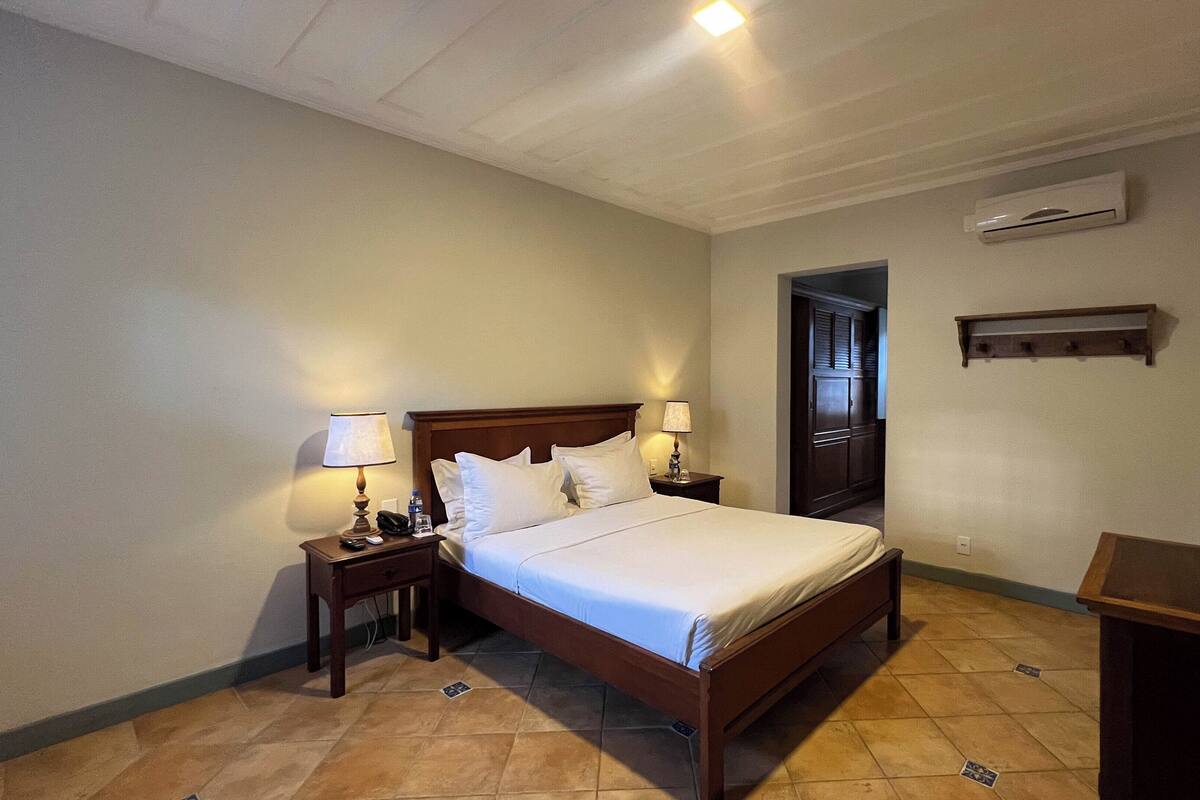 Habitación de hotel con una cama de madera, dos mesitas de noche con lámparas, un televisor de pantalla plana y un aire acondicionado de pared.