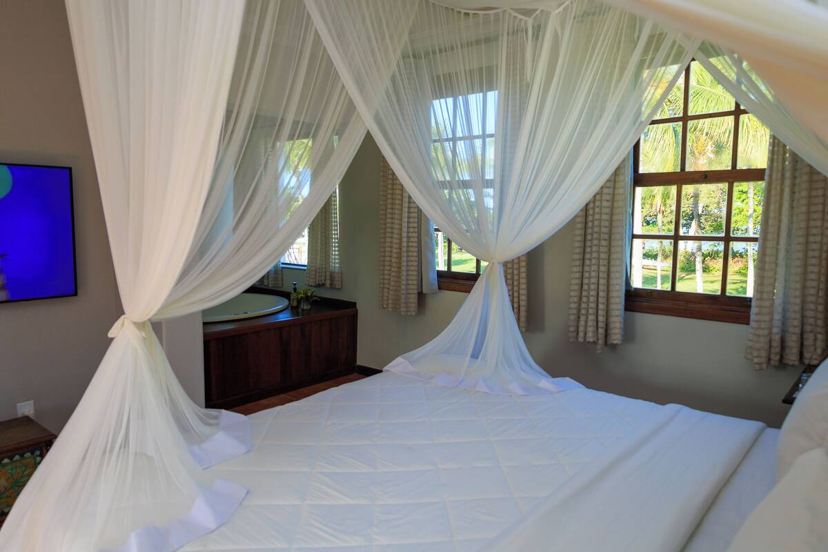 Un dormitorio con una cama grande, una mesita de noche, un espejo y una ventana con cortinas.