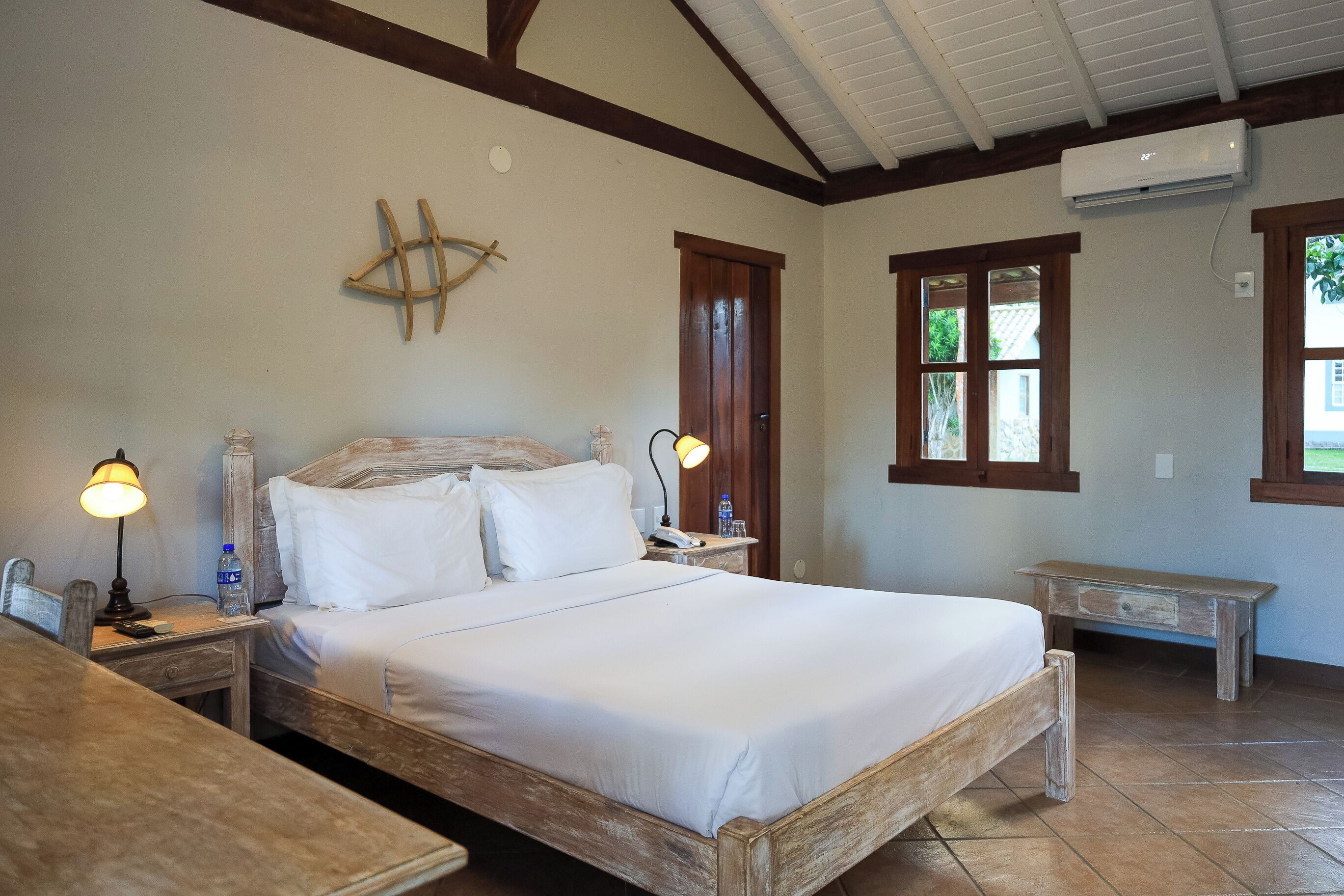 A well-lit bedroom with a wooden bed, bedside lamps, a wooden nightstand, and a small wooden bench.