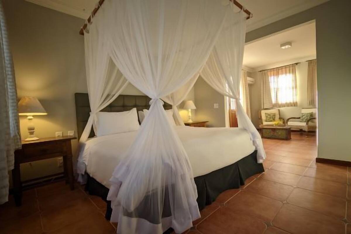 Un dormitorio con cama de dos plazas, una mesita de noche con lámpara y vistas a una sala de estar con sofá y mesa de centro.