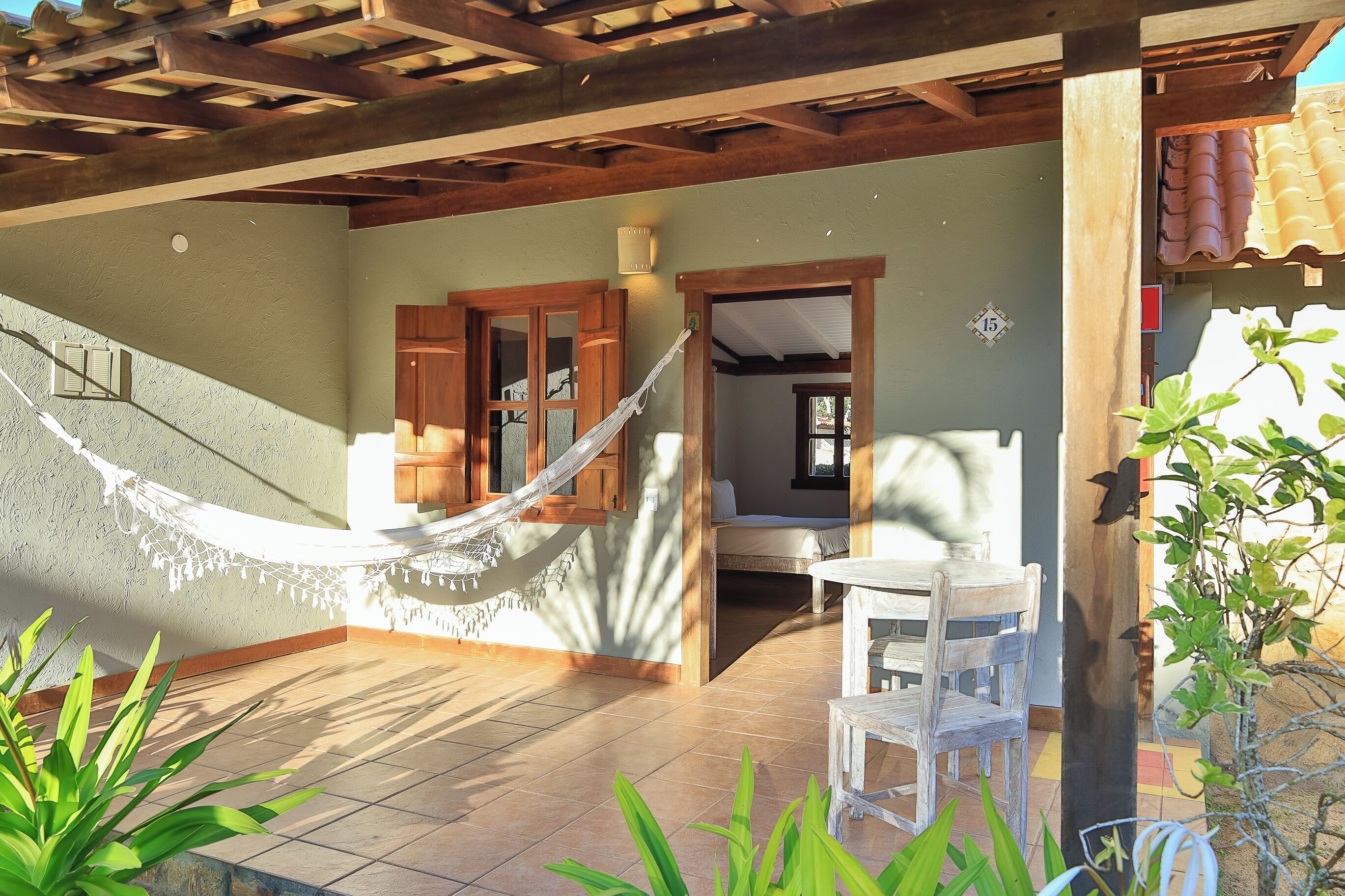 A covered patio with a hammock, wooden furniture, and a tiled floor.