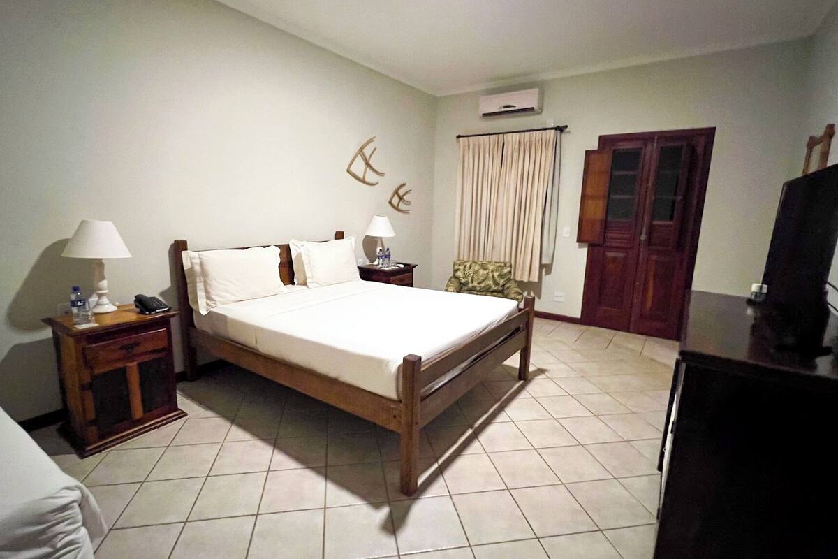Una habitación de hotel con una cama, dos mesitas de noche con lámparas, un armario y una televisión.