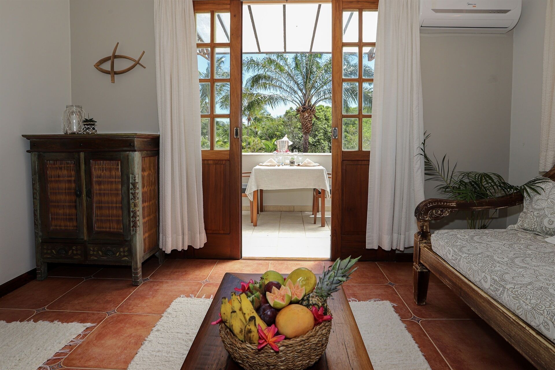 A room with a wooden cabinet, a dining table set for two, and a bed with a patterned bedspread.