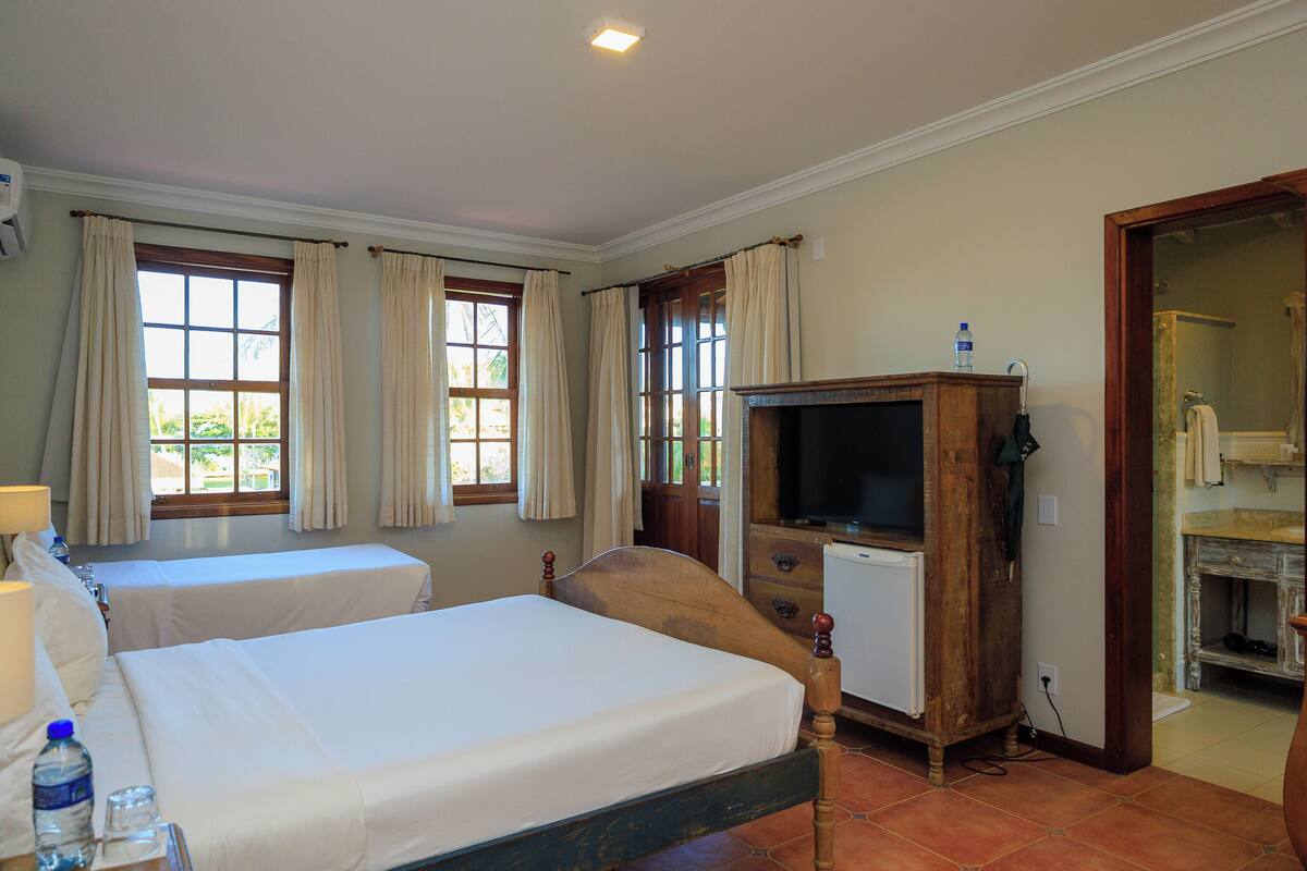 Habitación de hotel con dos camas, un televisor, un mueble de madera y un baño visible a través de una puerta abierta.