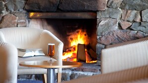 A cozy seating area with a stone fireplace, a round table, and a striped sofa. - Discovery Countrytime Hotel (Omarama)