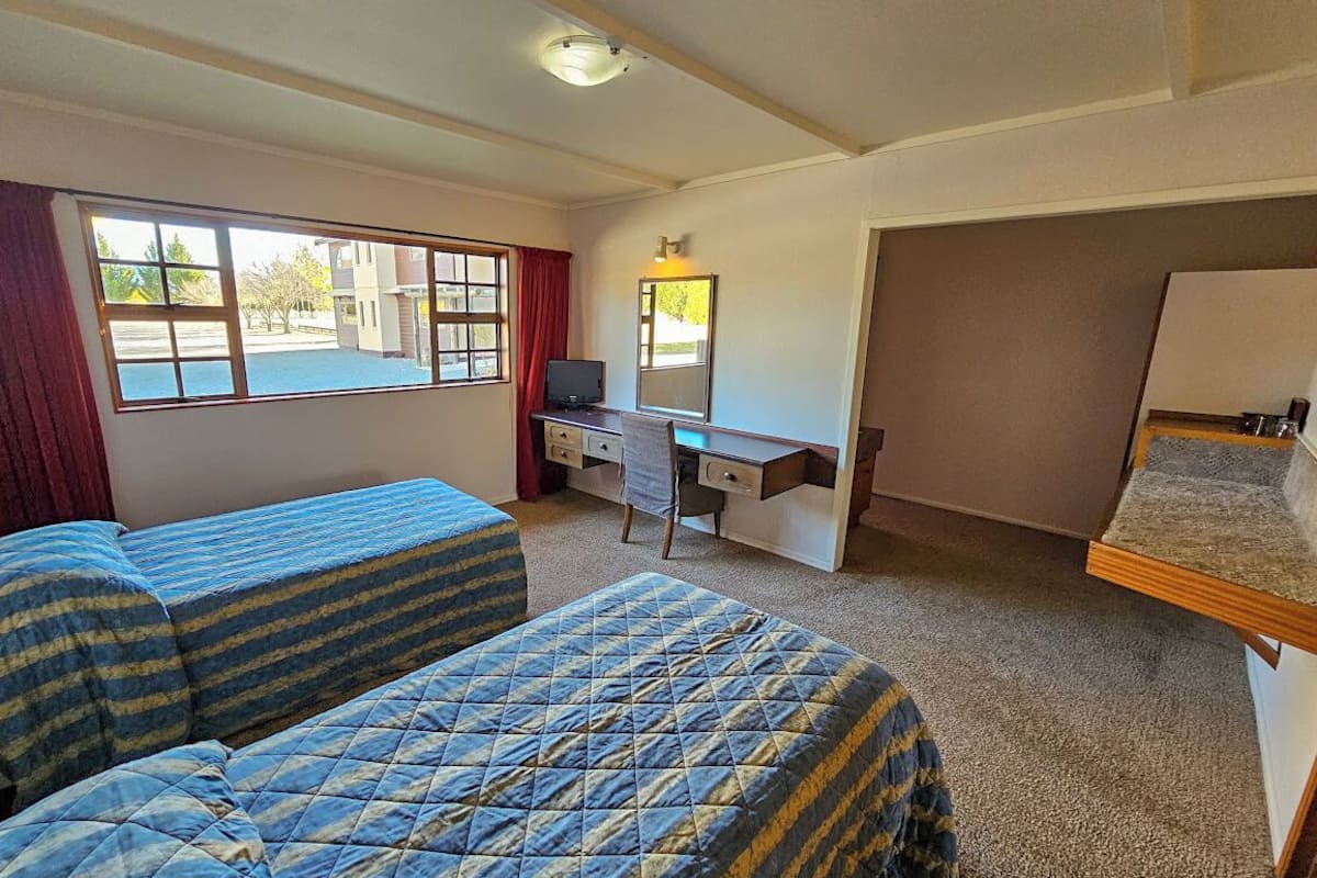 A room with two beds, a desk, a chair, and a television.