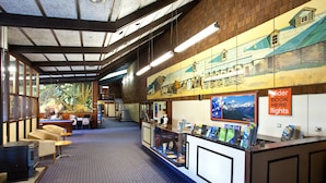 A reception area with a counter, seating, and a mural on the wall. - Discovery Countrytime Hotel (Omarama)