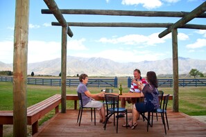 A wooden deck with a table and chairs, overlooking a grassy field and mountains. - Discovery Countrytime Hotel (Omarama)