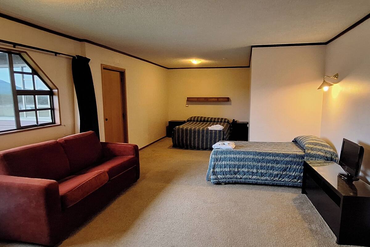 A compact hotel room with a single bed, a red sofa, a small table, and a TV.