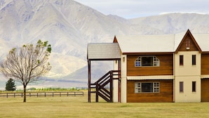 A two-story wooden house with a covered porch and a staircase leading to a deck. - Discovery Countrytime Hotel (Omarama)