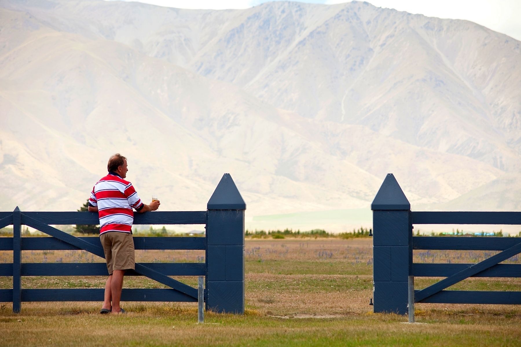 A person standing at a gate with a mountainous landscape in the background.