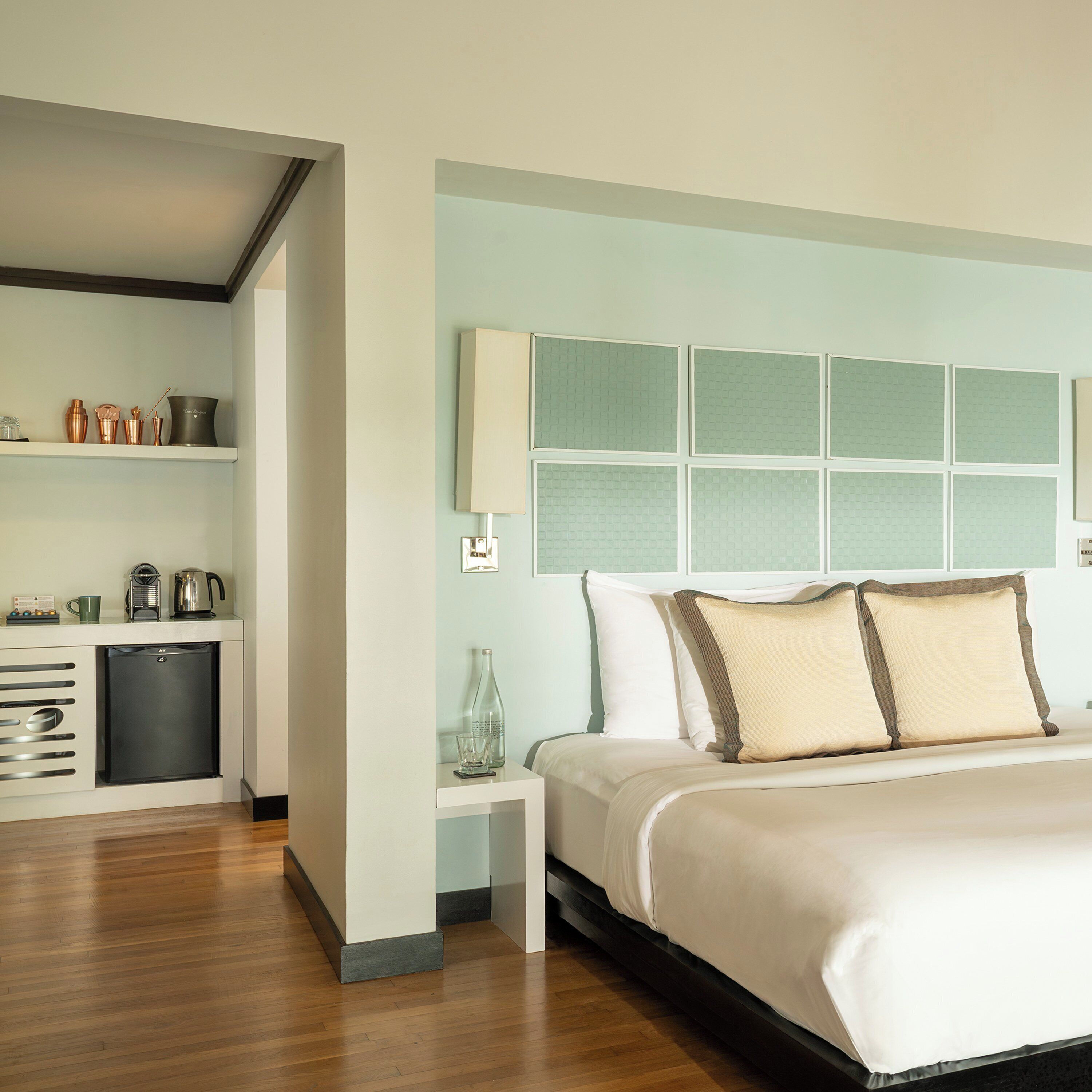 Una habitación de hotel con cama, mesita de noche y una zona de kitchenette.
