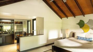 A modern hotel room with a kitchen area, a large bed with decorative pillows, and a ceiling fan.
