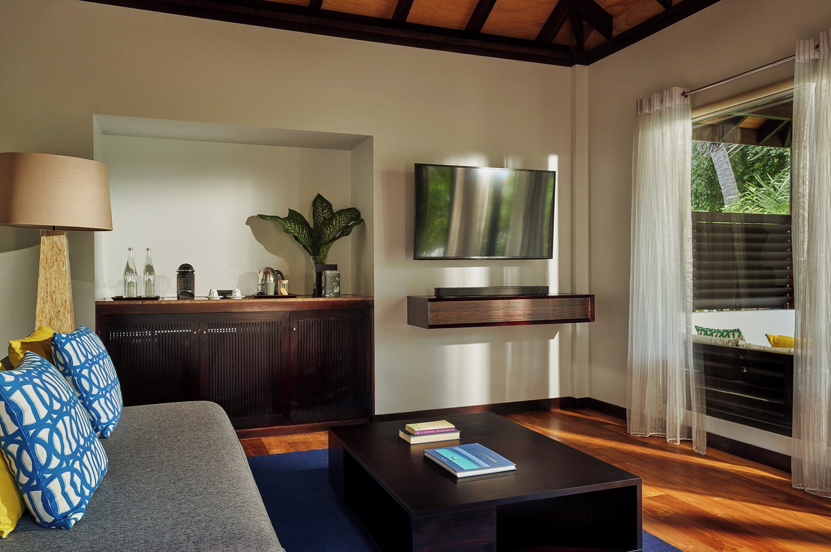 Una sala de estar moderna con sofá, mesa de centro, televisor y una planta.