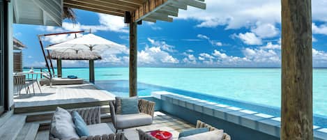 An outdoor lounge area with wooden flooring, cushioned seating, and a view of the ocean.
