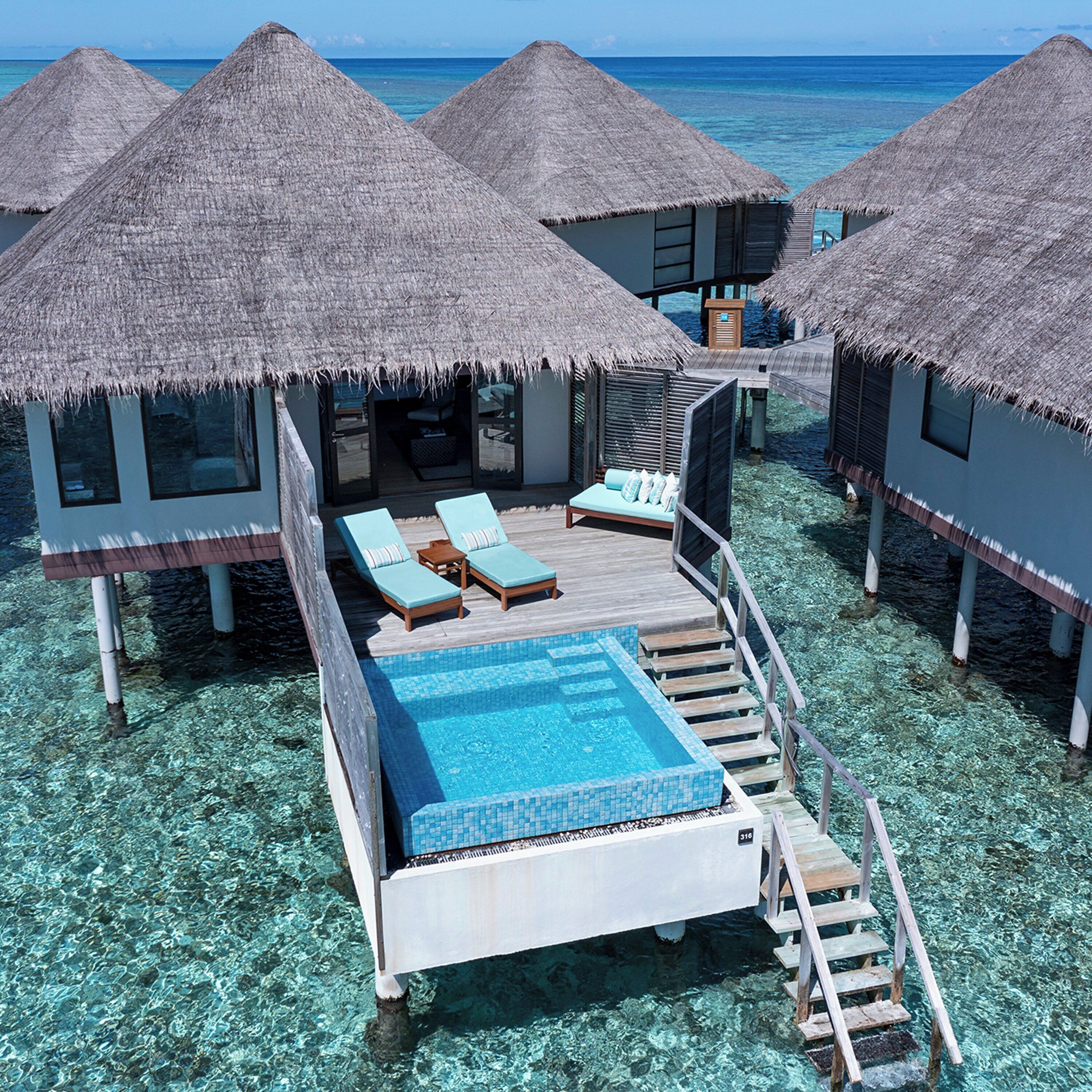Overwater bungalows with thatched roofs, a pool, and lounge chairs.