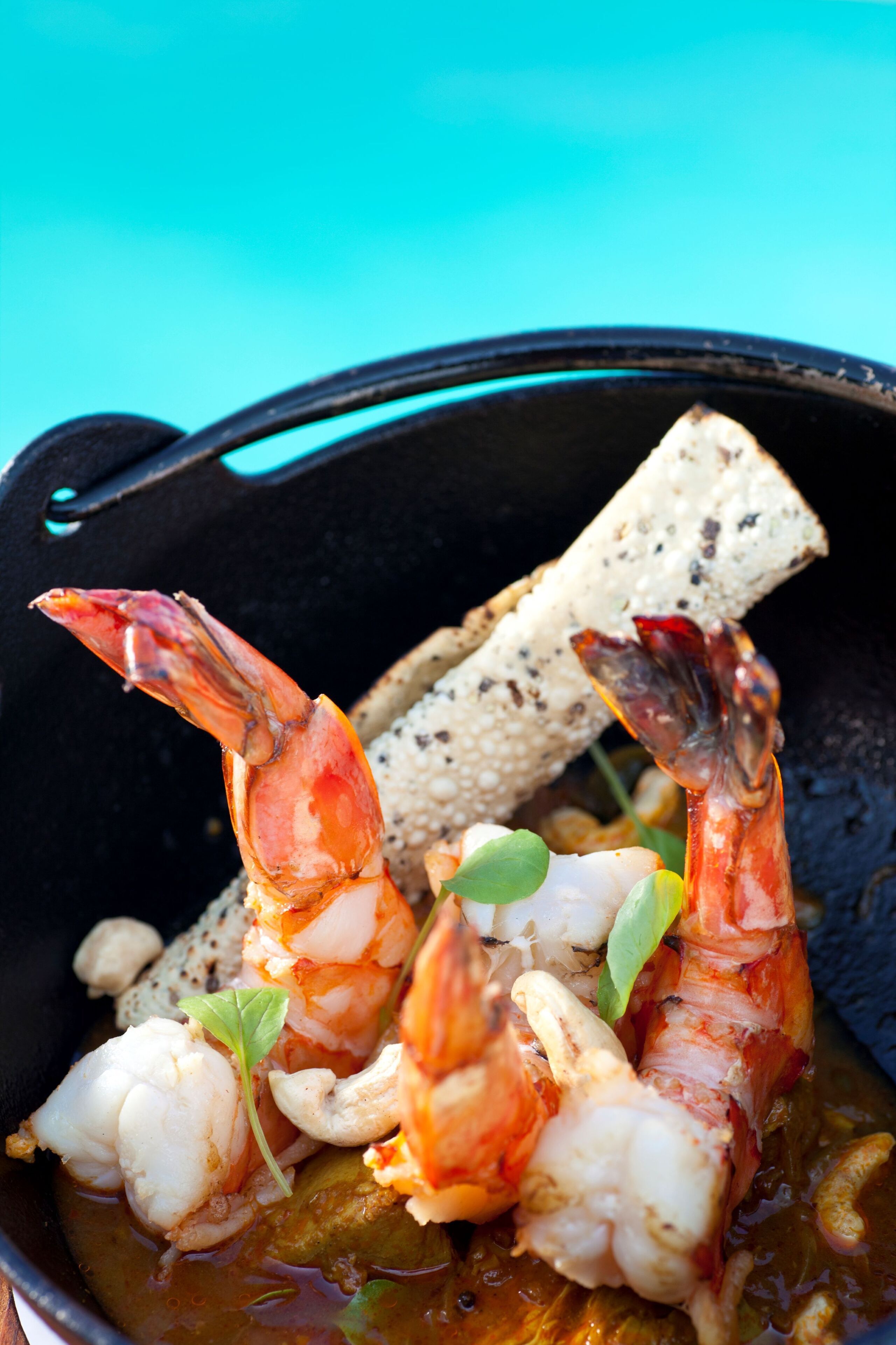 A bowl of seafood with shrimp and scallops, accompanied by crackers and a small green garnish.
