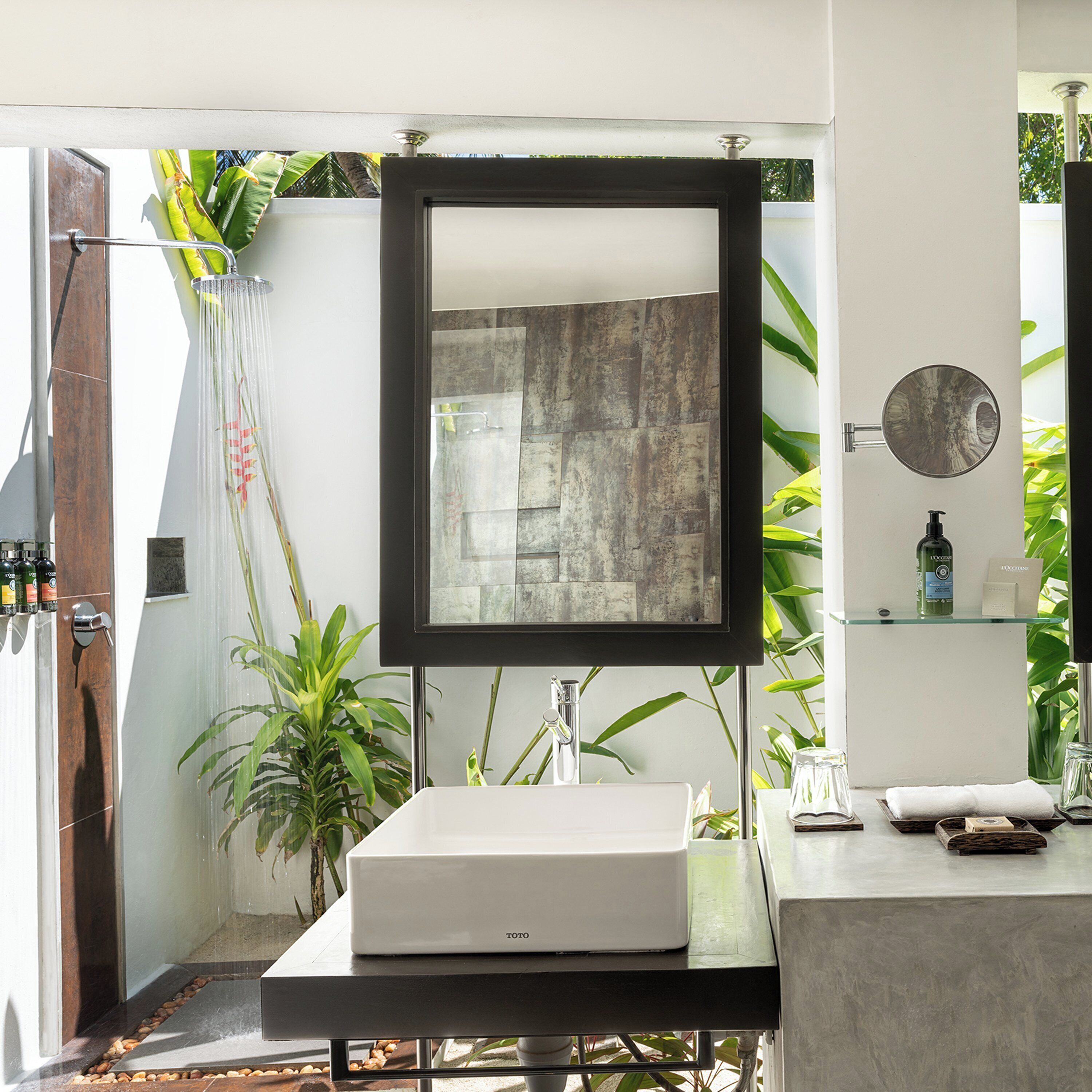 A modern bathroom with a large mirror, a white sink, and a glass shelf with toiletries.