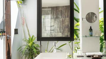 A modern bathroom with a large mirror, a white sink, and a glass shelf with toiletries.
