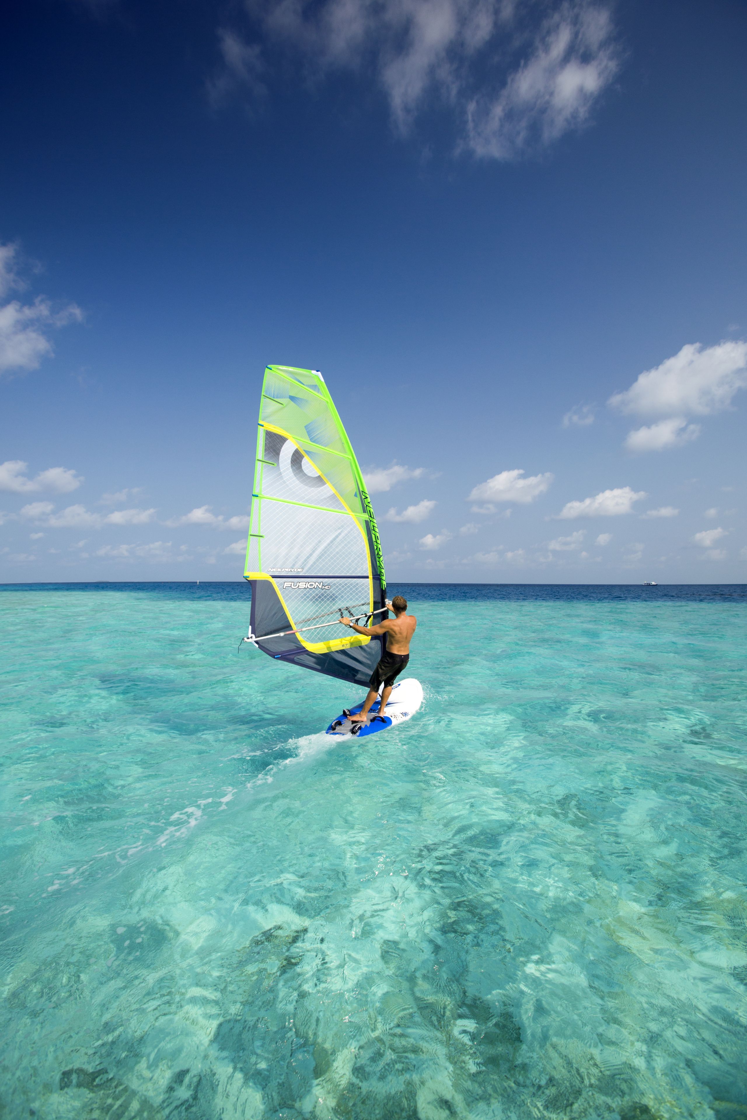 A person windsurfing in clear turquoise waters under a bright blue sky.